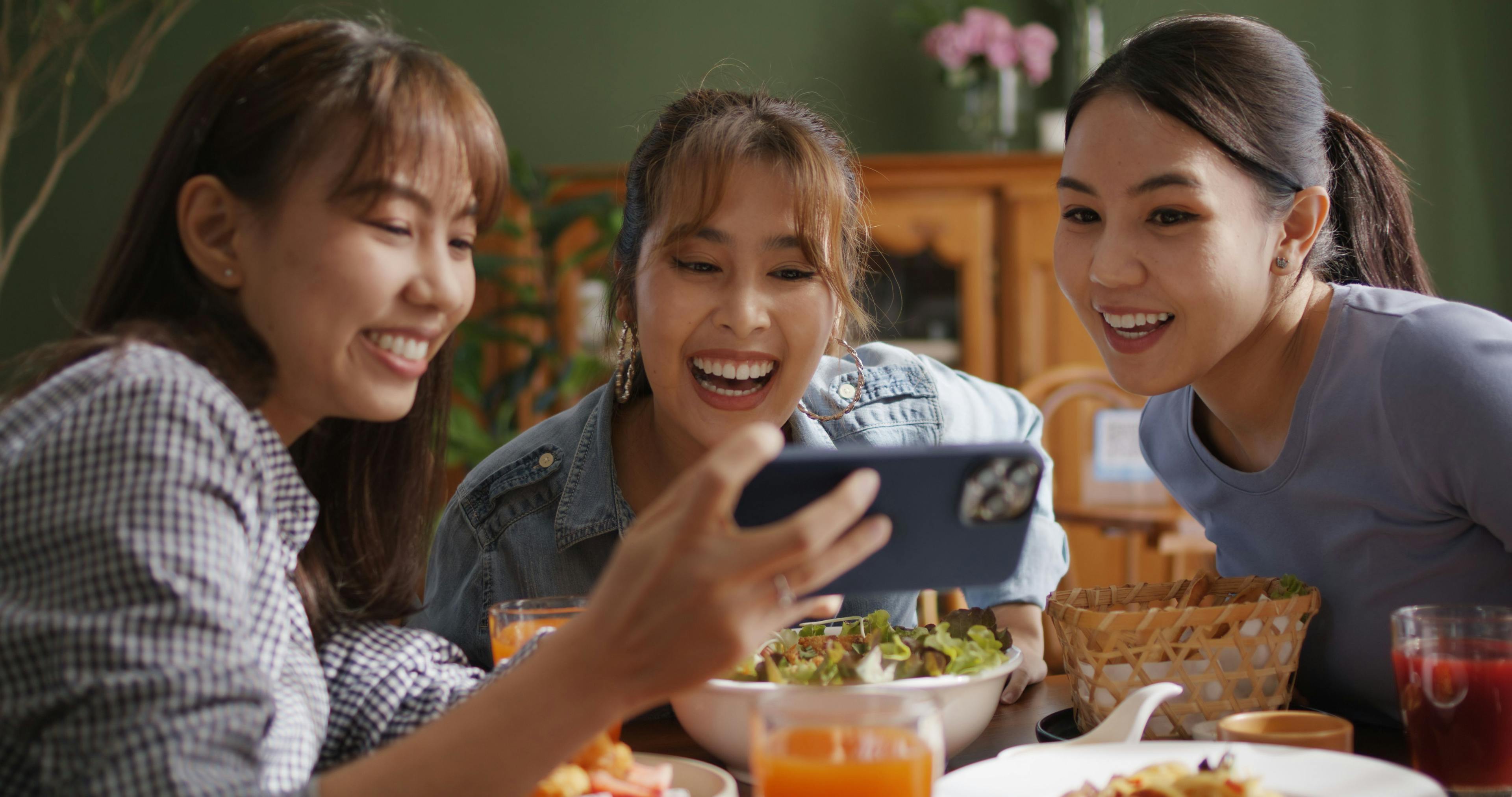 A delightful scene of three women smiling and using their cell phones to take a selfie, illustrating the essence of a TikTok guide for restaurants.